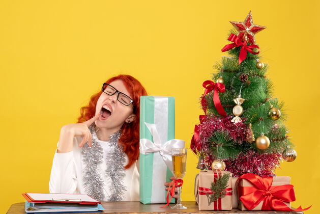 坐前视图：女医生拿着圣诞礼物和黄色背景上的圣诞树坐着女礼物快乐