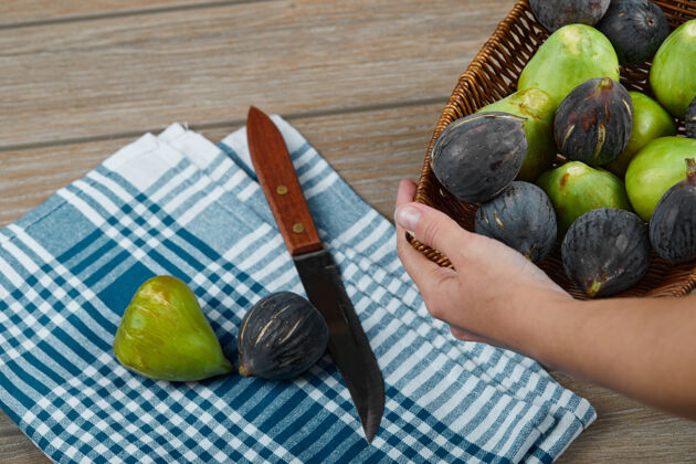绿色一只手拿着一篮子无花果放在木桌上 手里拿着刀和桌布季节性植物新鲜