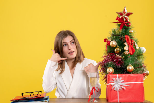 生活正面图：女医生坐在黄色背景的桌子前 放着圣诞树和礼品盒室内微笑坐