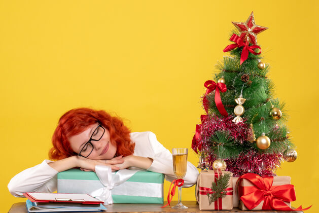 人前视图：女医生拿着圣诞礼物和黄色背景上的圣诞树坐着人圣诞树坐着