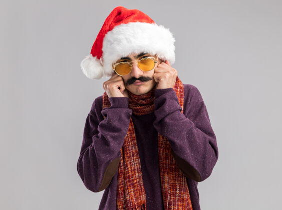 帽子留着胡子的男人戴着圣诞老人帽 戴着黄色眼镜 脖子上围着暖和的围巾 看上去既紧张又担心新的看着温暖