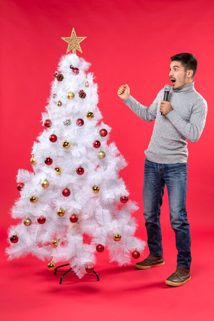 心情新年气氛积极的家伙穿着牛仔裤站在装饰圣诞树附近圣诞树站着圣诞节