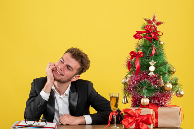 圣诞节正面图：坐在工作场所后面的男工人脸上露出黄色微笑地点男新郎
