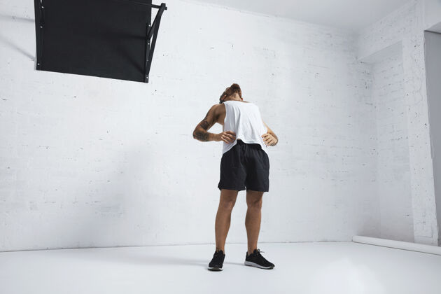 人运动纹身男子在白色空白坦克t恤伸展他的胸部和腹部锻炼后 隔离在砖墙 旁边的黑色拉杆美学运动员手臂
