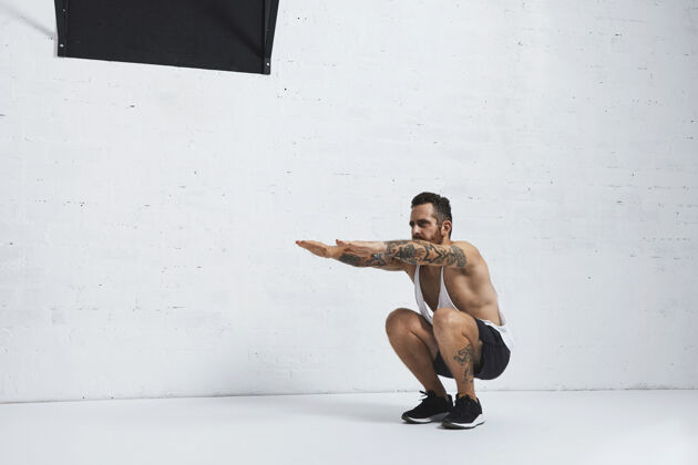 运动场强烈的纹身在白色无标签坦克t恤男运动员显示健美操动作蹲小腿上升 低位置健康运动运动装