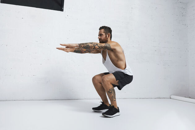 运动强烈的纹身在白色无标签坦克t恤男运动员显示健美操动作蹲持板运动男性健身房训练