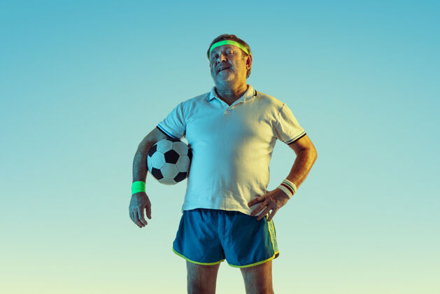 男穿运动服在渐变背景和霓虹灯下踢足球的资深男士活跃业余健康