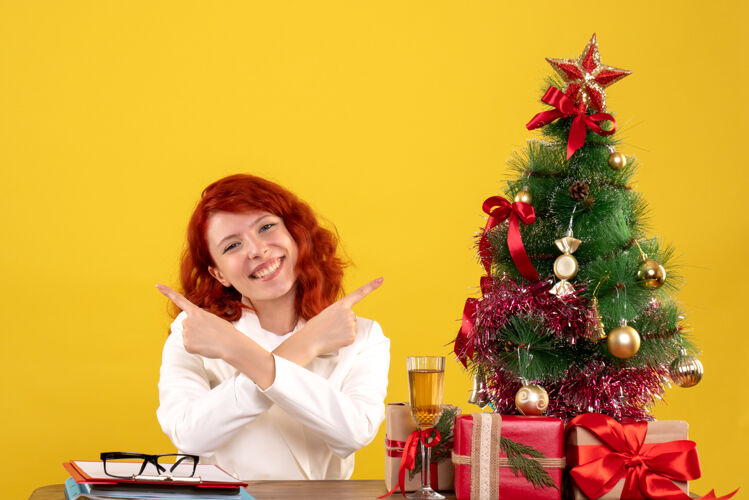 桌子女工人坐在桌子后面 黄色桌子上放着圣诞礼物和圣诞树圣诞节树坐着