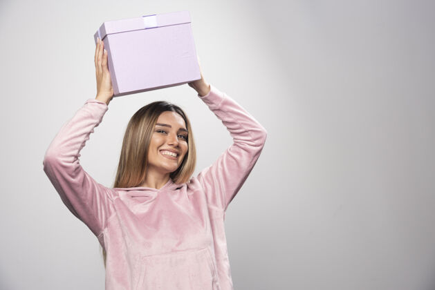 女士一位身穿粉色运动衫的金发女士头上举着一个礼盒 颤抖着礼物成人年轻