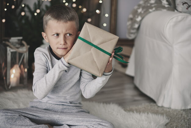 房间男孩摇着包好的礼物看礼物盒圣诞礼物