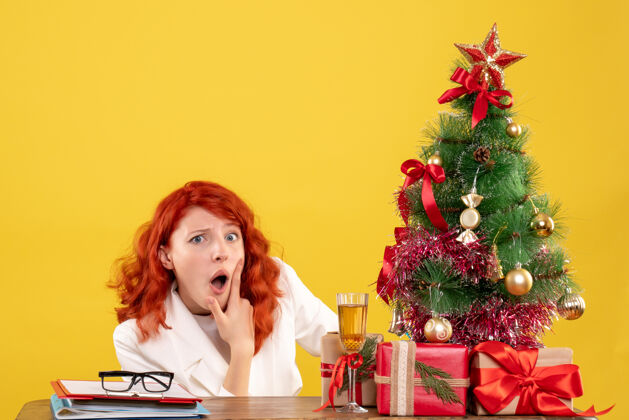 花前视图：女医生坐在桌子后面 黄色背景上有圣诞礼物坐着医生背景