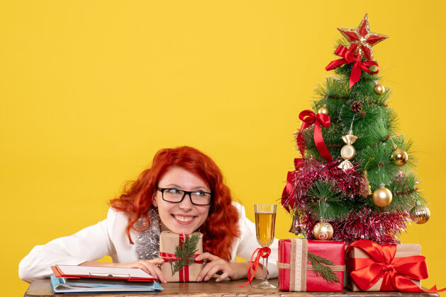 微笑前视图：女医生坐在桌子后面 黄色背景上有圣诞礼物快乐圣诞节医生