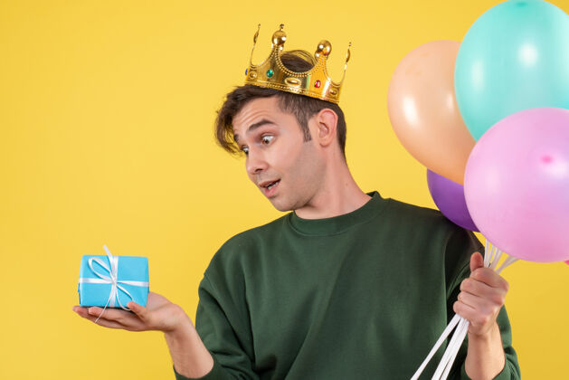 成人正面图帅哥戴着皇冠拿着气球看黄色的礼物工作年轻期待
