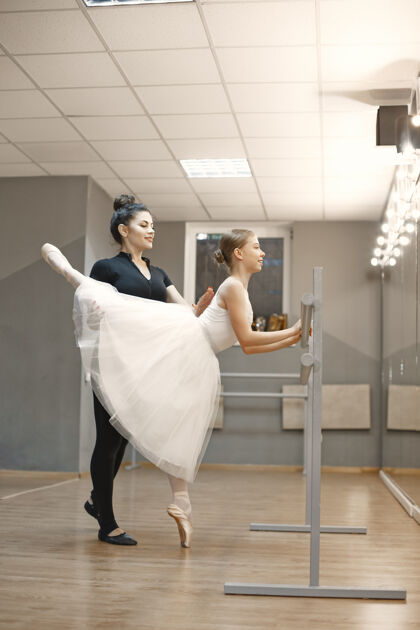 姿势穿着白色芭蕾舞服装的可爱的小芭蕾舞演员年轻的女士在房间里跳舞和老师一起上舞蹈课的女孩人教育工作室