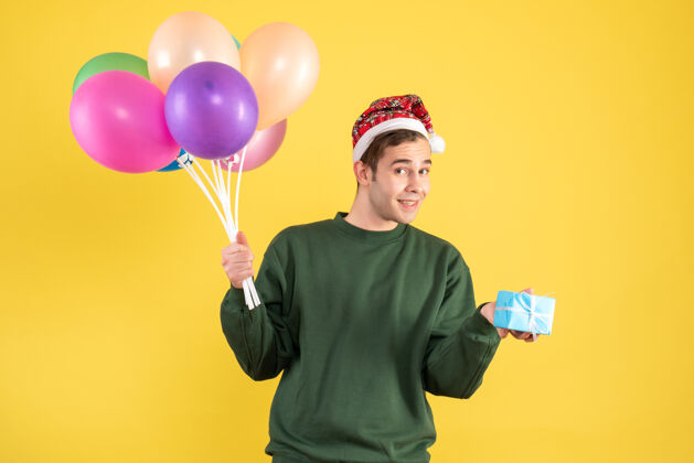 快乐正面图快乐的年轻人戴着圣诞帽 站在黄色的气球上男人吹着圣诞老人