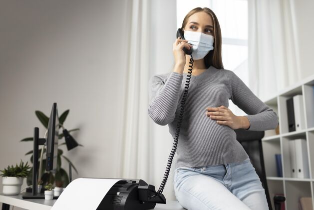 女性戴着医用口罩的孕妇在办公室接电话母亲母亲孕妇