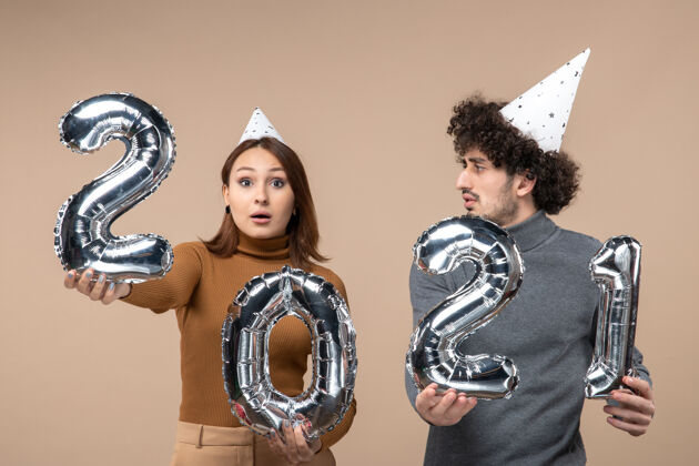 帽子体贴的年轻夫妇戴着新年帽摆出姿势 镜头里的女孩和穿灰色衣服的男人肖像年轻夫妇黄铜