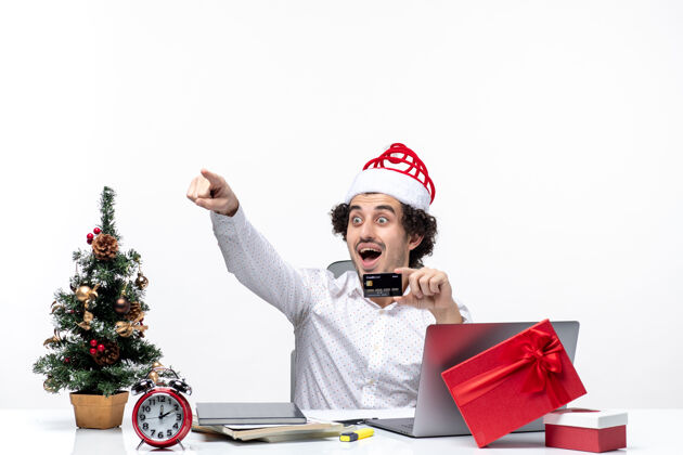 帽子戴着圣诞老人帽子 拿着银行卡的商人在办公室里惊讶地看着并指着什么东西人业务人员人