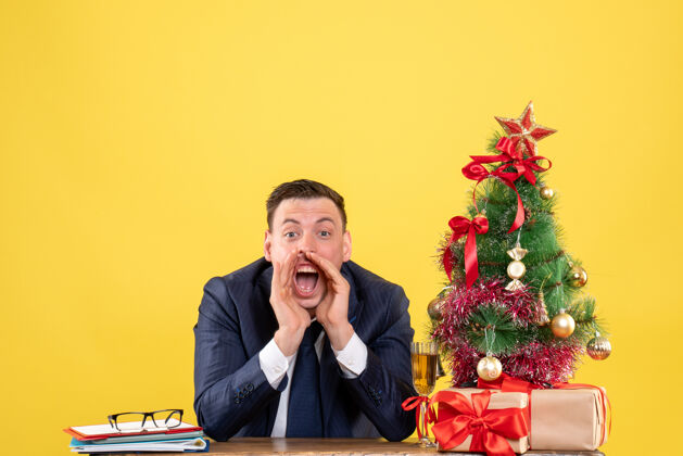 人圣诞树旁的桌子上坐着一个大声喊叫的男人 黄色的礼物肖像西装商人