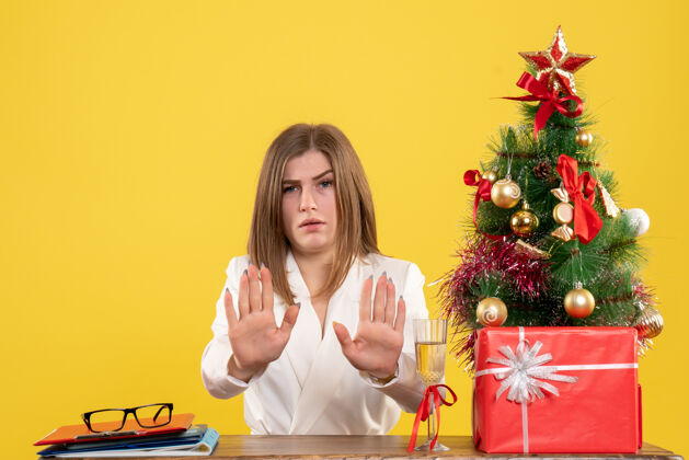 前面正面图：女医生坐在黄色背景的桌子前 放着圣诞树和礼品盒办公室医生健康