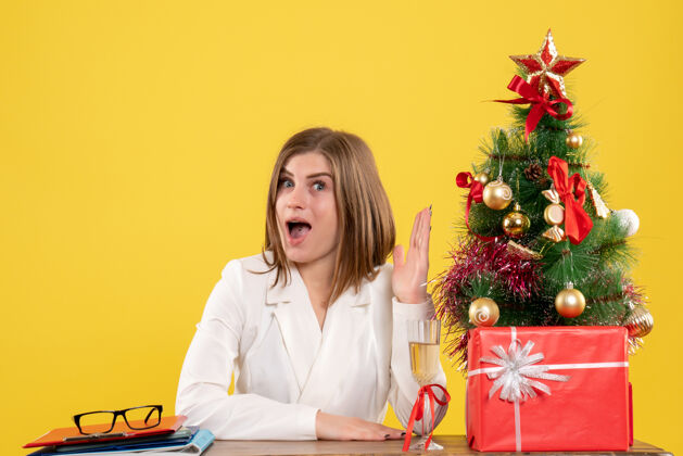 桌子正面图：女医生坐在黄色背景的桌子前 放着圣诞树和礼品盒工作医院背景