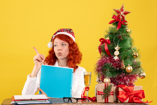 女医生正面图：女医生坐在桌子后面 手里拿着文件 背景是黄色的圣诞树和礼盒文件医生人