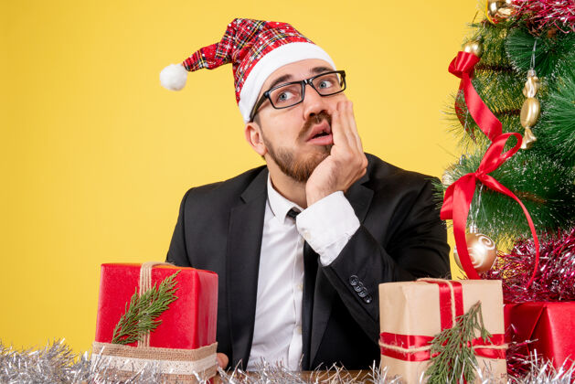 圣诞节前面近距离看男工人围坐在礼物和小树上思考黄色周围礼物坐
