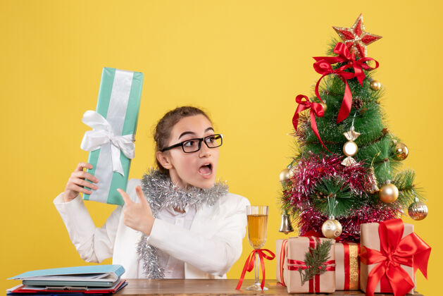 前面前视图女医生围坐在圣诞礼物和树上拿着黄色背景上的礼物礼物抱着人