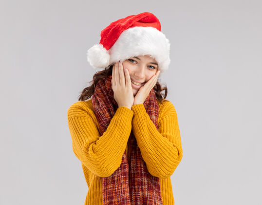 脸戴着圣诞帽 脖子上围着围巾的年轻斯拉夫姑娘高兴地把手放在脸上空间圣诞快乐女孩