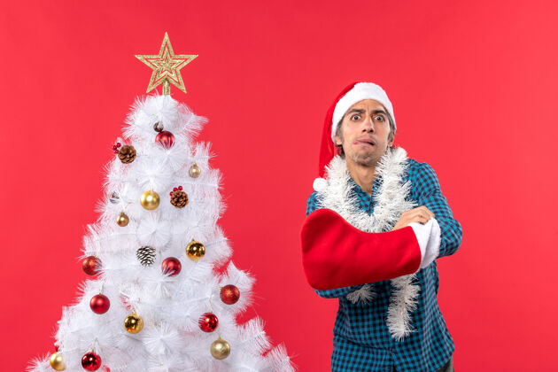 圣诞老人一个戴着圣诞老人帽子 穿着蓝色条纹衬衫的紧张的年轻人年轻人圣诞树袜子
