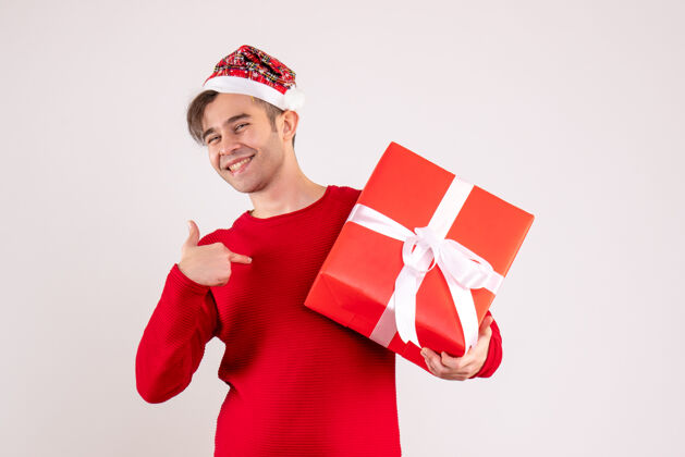 礼物正面图快乐的年轻人戴着圣诞老人的帽子指着自己的白色庆祝丝带纸