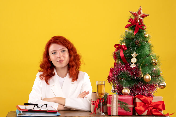 办公室女工人坐在桌子后面 手里拿着圣诞礼物和黄色的圣诞树树主任圣诞节