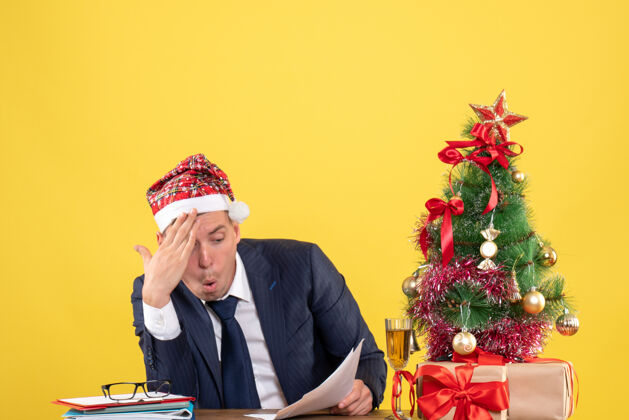坐着在圣诞树旁的桌子旁 一个好奇的男人正在检查文件 黄色的礼物礼物好奇的人礼物