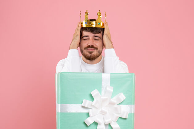 年轻年轻人在礼物盒内的正面视图 粉红色墙上有皇冠里面纸人
