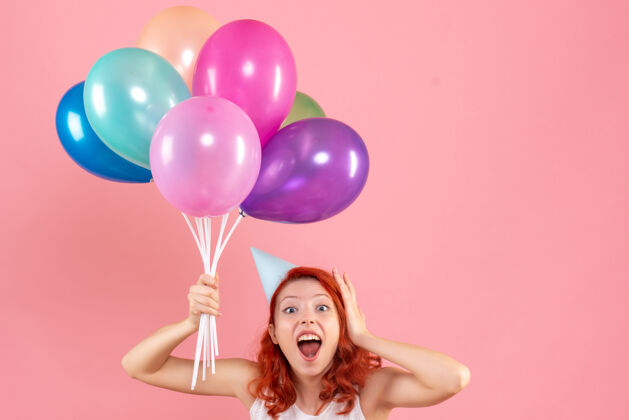 前面一位年轻女子手持彩色气球站在粉色墙上的正面照片女人举行聚会