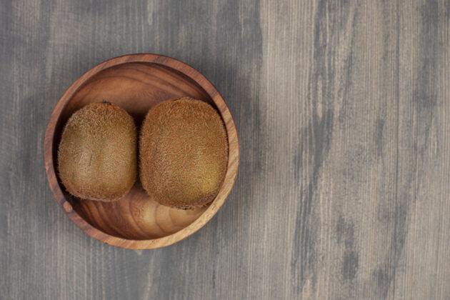 新鲜木桌上放着一个木碗和两个新鲜的猕猴桃高质量的照片猕猴桃食物水果