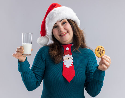 牛奶微笑的成年白人妇女戴着圣诞帽 打着圣诞领带 手里拿着一杯牛奶和饼干 背景是白色的 有复印空间成人微笑杯子