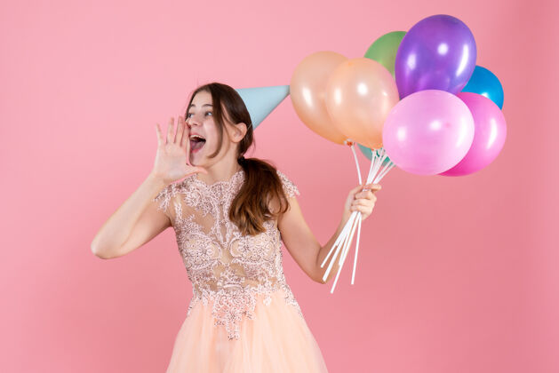 乐趣戴着派对帽的派对女孩拿着气球向穿粉红色衣服的人打招呼气球帽子聚会
