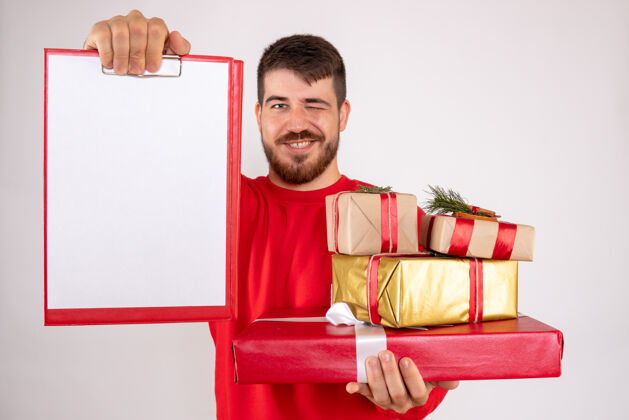 举行身穿红衫的年轻人拿着圣诞礼物 在白色的墙上贴着纸条人们文件微笑
