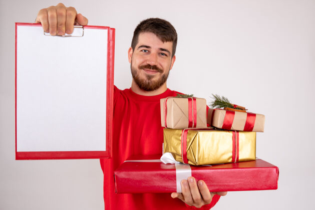 微笑身穿红衫的年轻人拿着圣诞礼物和白墙上的文件说明的正面视图男性举行人们