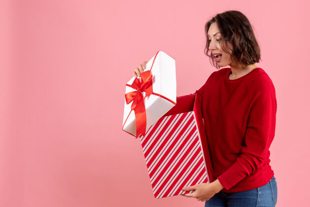 漂亮年轻女子在粉红色墙上打开礼物的正面图礼物正面情感