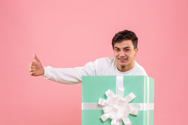 礼品盒隐藏在粉红色墙上的礼物里面的年轻人的正面视图人类人年轻男性