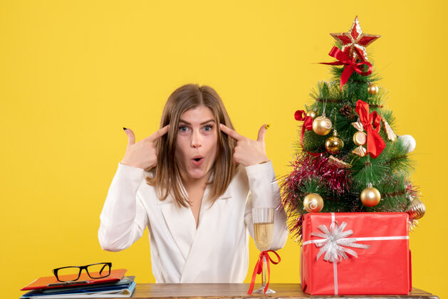 圣诞节正面图：女医生坐在黄色背景的桌子前 放着圣诞树和礼品盒桌子医生健康