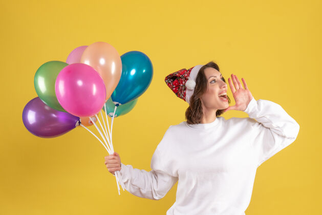 快乐黄色墙壁上手持彩色气球的年轻女子的正视图气球情感举行