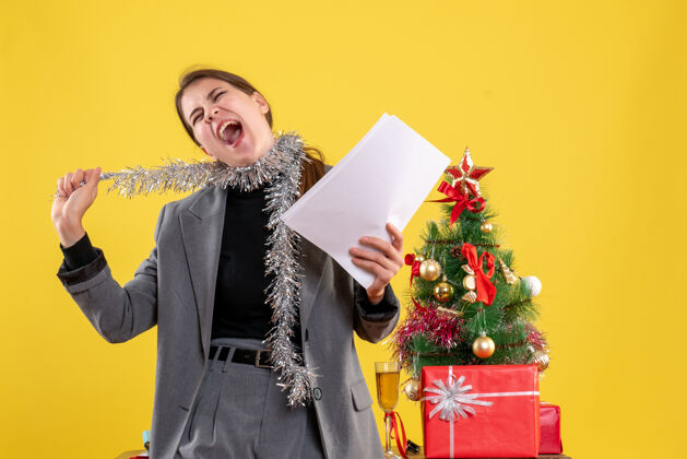 女孩前视图喊着可爱的女孩拿着文件站在圣诞树和礼物鸡尾酒附近人靠近圣诞节