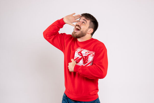 年轻男性一个穿着红衫的年轻人在白色的墙上举着圣诞礼物的正视图男性情感人