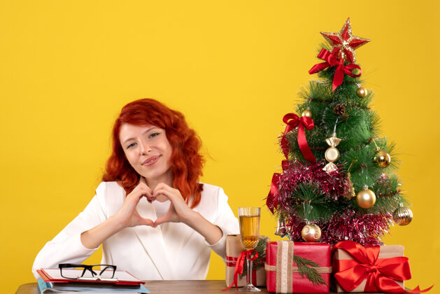 礼物女工人坐在桌子后面 手里拿着圣诞礼物和黄色的圣诞树女工人情感安排