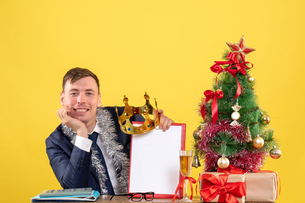 桌子笑眯眯的帅哥坐在圣诞树旁的桌子前 黄色的礼物微笑树坐着