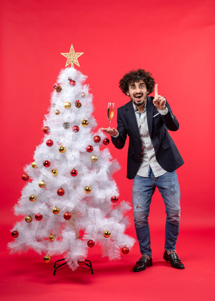 庆祝有胡子的年轻人拿着酒庆祝新年 他站在装饰好的白色圣诞树旁站着酒男人