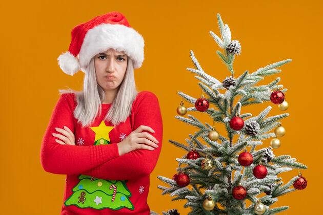女人愤愤不平的金发女郎 穿着圣诞毛衣 戴着圣诞帽 眉头紧锁 双臂交叉胳膊站着皱眉